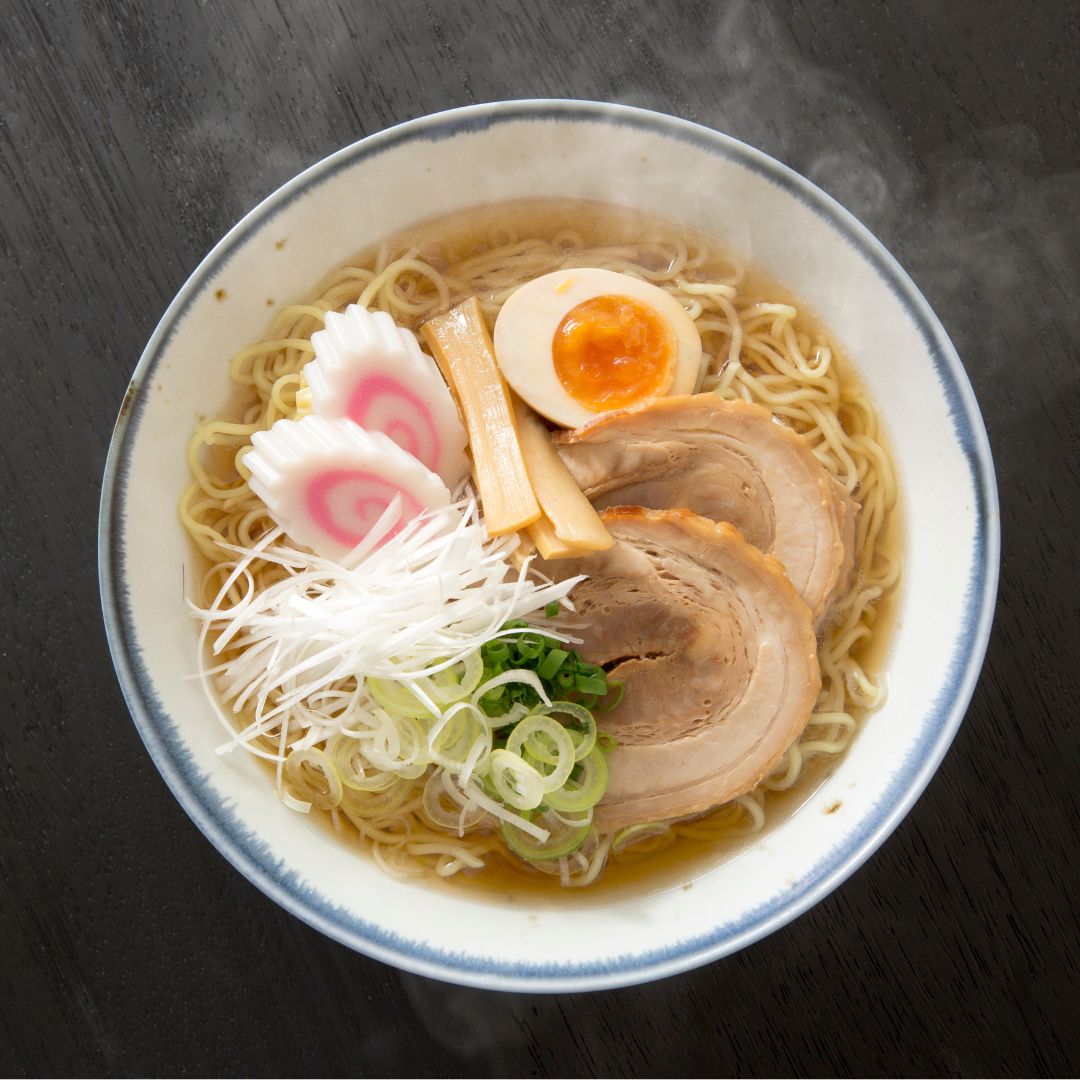 Ein heisses dampfendes leckeres Ramengericht mit Naruto, Lauch, Ei und Menma in einer Ramen Brühe aus Shoyu in einer weissen Schüssel von oben