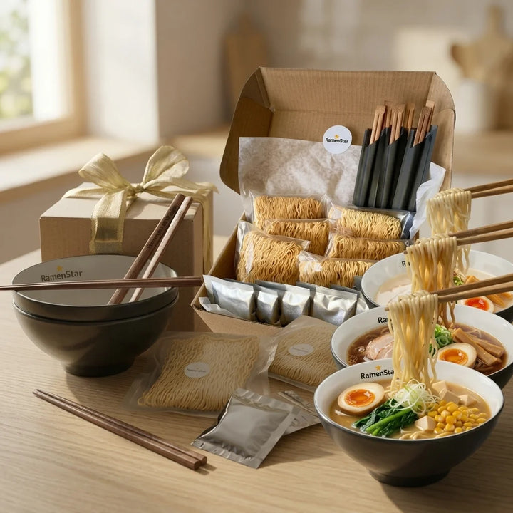 RamenStar-Geschenkset auf einem Holztisch, bestehend aus einer offenen Box mit verpackten Ramennudeln und Soßen, einer Geschenkbox mit Goldschleife, leeren Schalen und drei fertigen Ramenschalen mit verschiedenen Belägen wie Fleisch, Ei, Mais und Tofu. Essstäbchen heben Nudeln aus den Schalen.