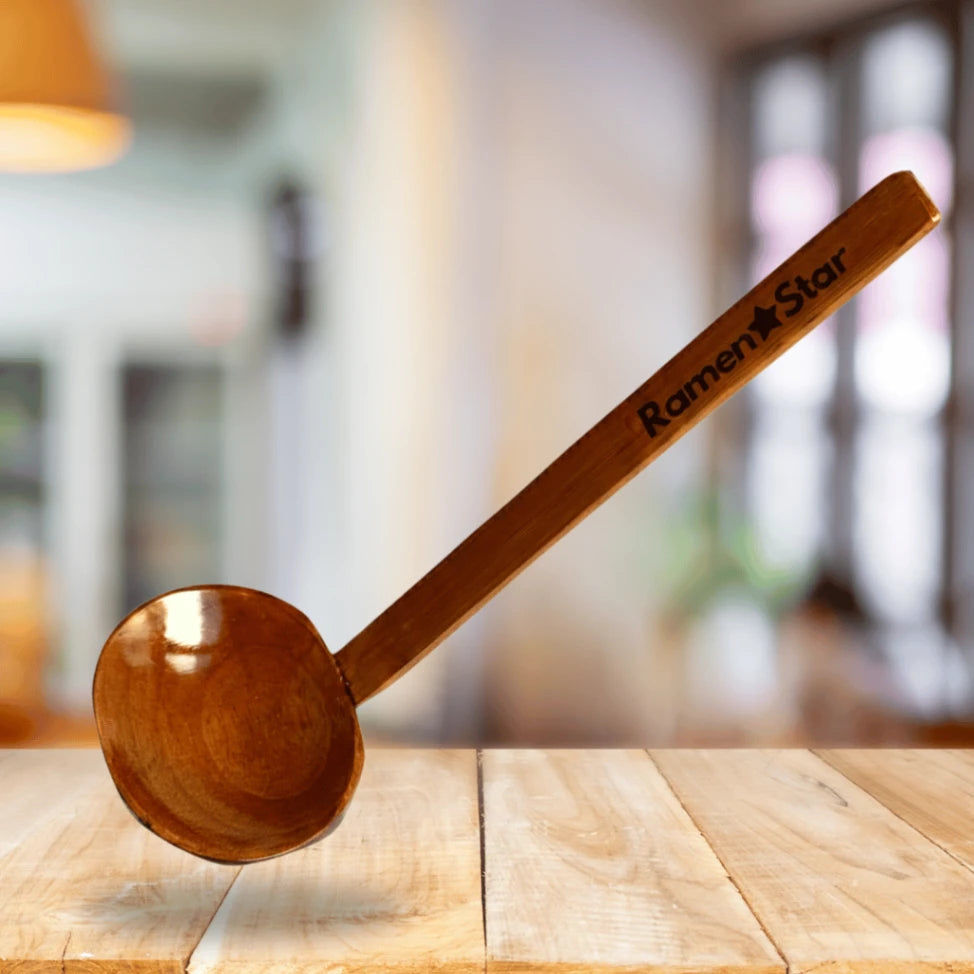 Ein hochwertiger, dunkler Holzlöffel mit glänzender Oberfläche, darauf der Markenname "Ramen Star" eingraviert, schwebt über einem hellen Holztisch. Perfekt für authentische Ramen-Suppen in japanischen Restaurants.