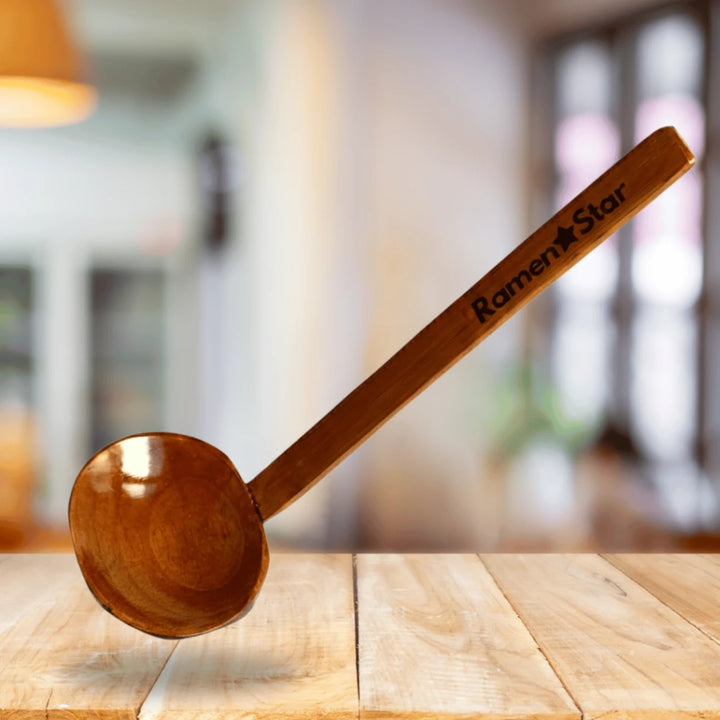 Ein hochwertiger, dunkler Holzlöffel mit glänzender Oberfläche, darauf der Markenname "Ramen Star" eingraviert, schwebt über einem hellen Holztisch. Perfekt für authentische Ramen-Suppen in japanischen Restaurants.