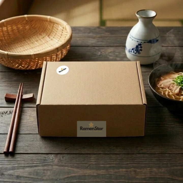 Braune RamenStar Lieferbox mit Logo auf dunklem Holztisch, daneben dampfende Schale Ramen mit Schweinefleisch und Frühlingszwiebeln, Essstäbchen, Sake-Karaffe und Bambuskorb, deutet auf authentisches japanisches Mahl zu Hause hin.
