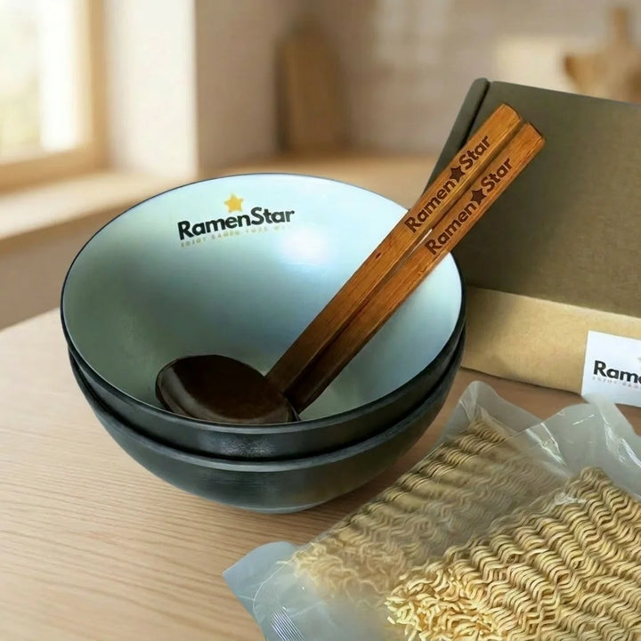 Dunkle RamenStar Nudelschalen mit weißer Innenseite und gelbem Markenlogo auf einer hellen Marmorarbeitsplatte, kombiniert mit passenden Holzstäbchen. Ein Stapel von drei weiteren Schalen steht im Hintergrund, bereit für asiatische Gerichte.