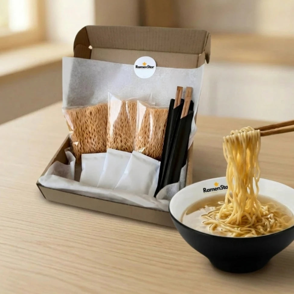 RamenStar DIY Ramen Kit in geöffneter Box, mit Nudelpaketen, Gewürzen und Essstäbchen. Daneben werden goldene Ramen-Nudeln mit Stäbchen aus einer schwarzen Schale mit dampfender Brühe gehoben, bereit zum Genuss.