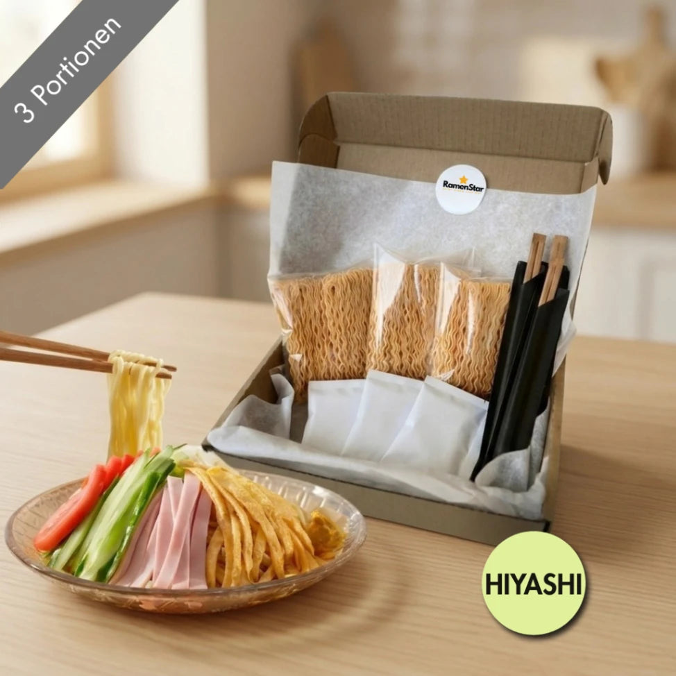Ein appetitliches RamenStar Hiyashi Chuka Ramen-Kit für drei Portionen, das eine angerichtete Schale mit kalten Nudeln, Gurke, Tomate, Schinken und Omelett zeigt, daneben die offene Box mit allen verpackten Zutaten und Essstäbchen.