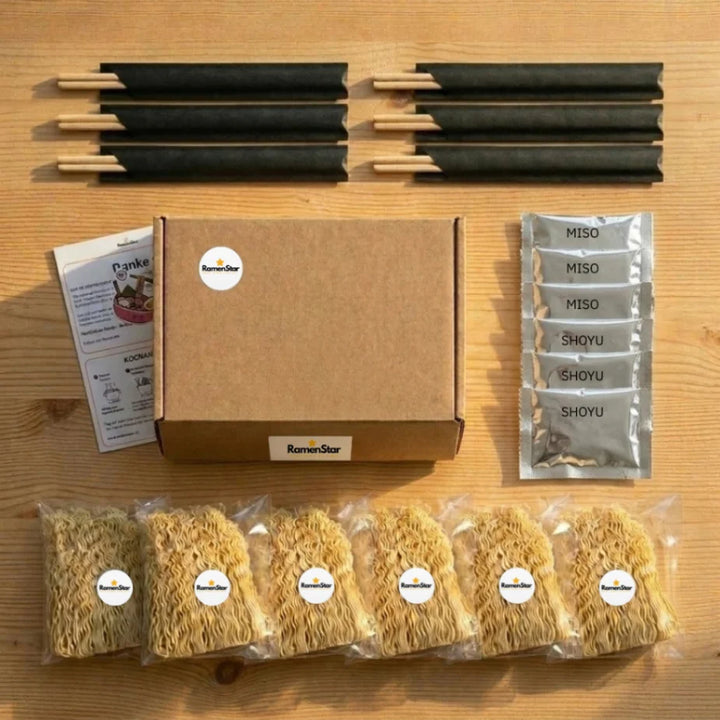 Detailansicht der RamenStar Kochbox auf einem Holztisch, mit brauner Versandbox, sechs Packungen getrockneter Ramen-Nudeln, drei Miso- und drei Shoyu-Saucenpäckchen sowie sechs Paar Essstäbchen für ein authentisches japanisches Mahl.
