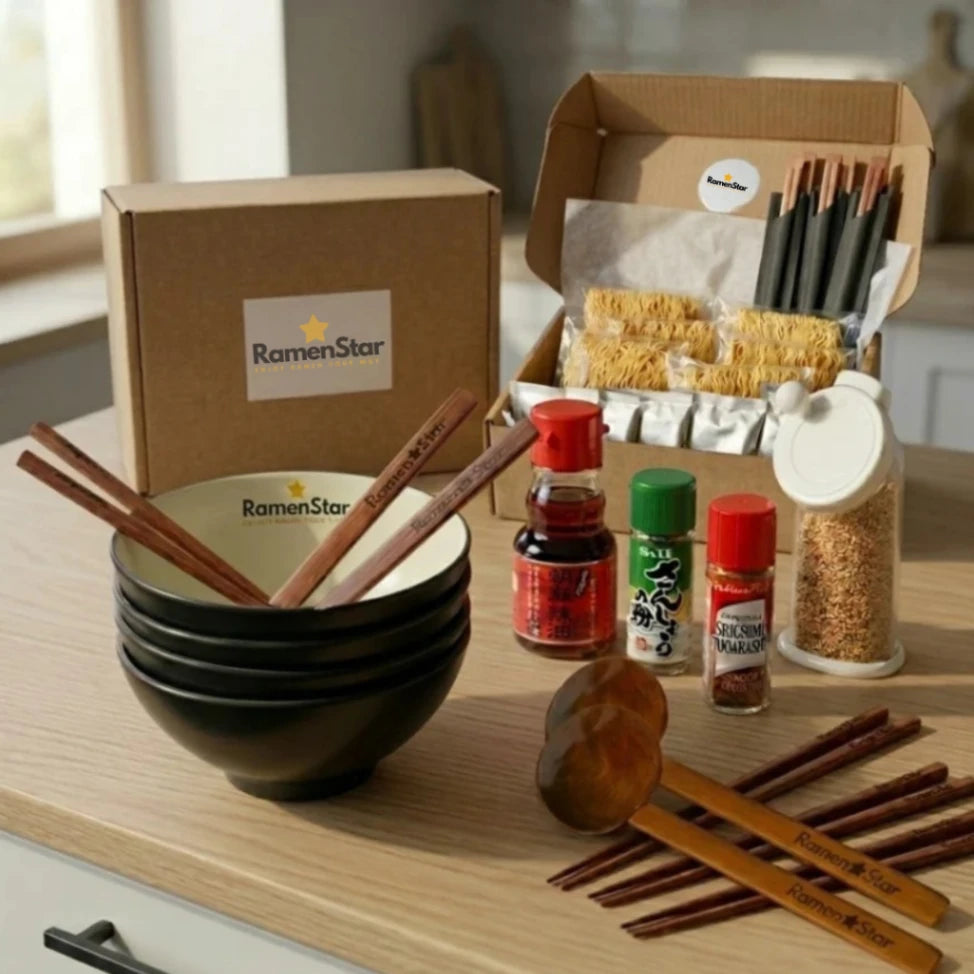 Ein umfassendes RamenStar-Koch-Kit präsentiert auf einer hellen Küchenarbeitsplatte, inklusive einer offenen Box mit Ramen-Nudeln und Gewürzsachets, vier schwarzen Ramen-Schalen mit passenden Holzstäbchen und Löffeln, sowie verschiedenen Gewürzflaschen für authentischen japanischen Ramen-Genuss zu Hause.