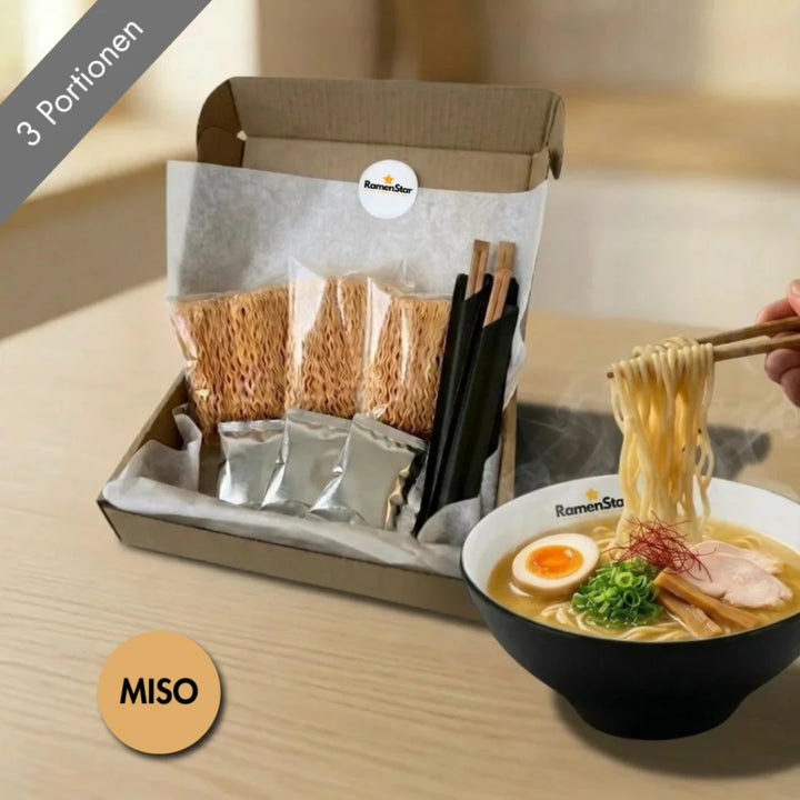 Ein offenes RamenStar Miso Ramen Essenspaket für drei Portionen mit Nudeln, Brühe und Stäbchen, präsentiert neben einer dampfenden Schüssel fertig zubereiteter Miso Ramen mit Ei, Huhn, Lauch und Chili-Fäden, von der Nudeln hochgehoben werden.