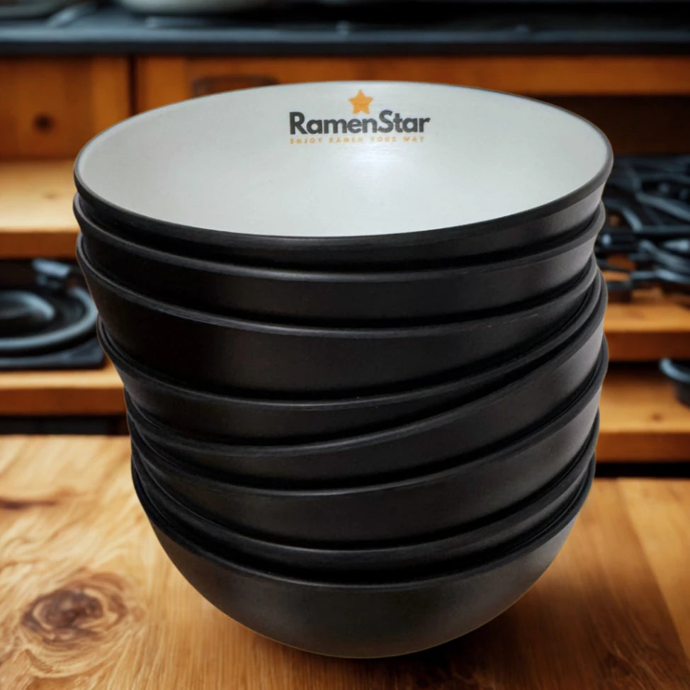 Ein Stapel eleganter, mattschwarzer Ramen-Schüsseln mit weißer Innenseite und dem goldgelben RamenStar-Logo, inklusive &