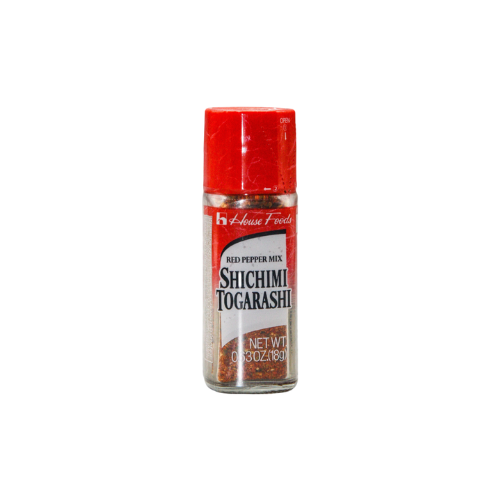 Das Bild zeigt eine kleine Glasflasche mit rotem Kunststoffdeckel, gefüllt mit der japanischen Gewürzmischung Shichimi Togarashi. Die Verpackung trägt die Aufschrift „Red Pepper Mix“ sowie das Markenlogo „House Foods“. Durch das Glas sind die feinen roten und orangen Gewürzanteile sichtbar. Die Mischung wird traditionell als scharfes Topping für Ramen, Udon oder Reis verwendet.
