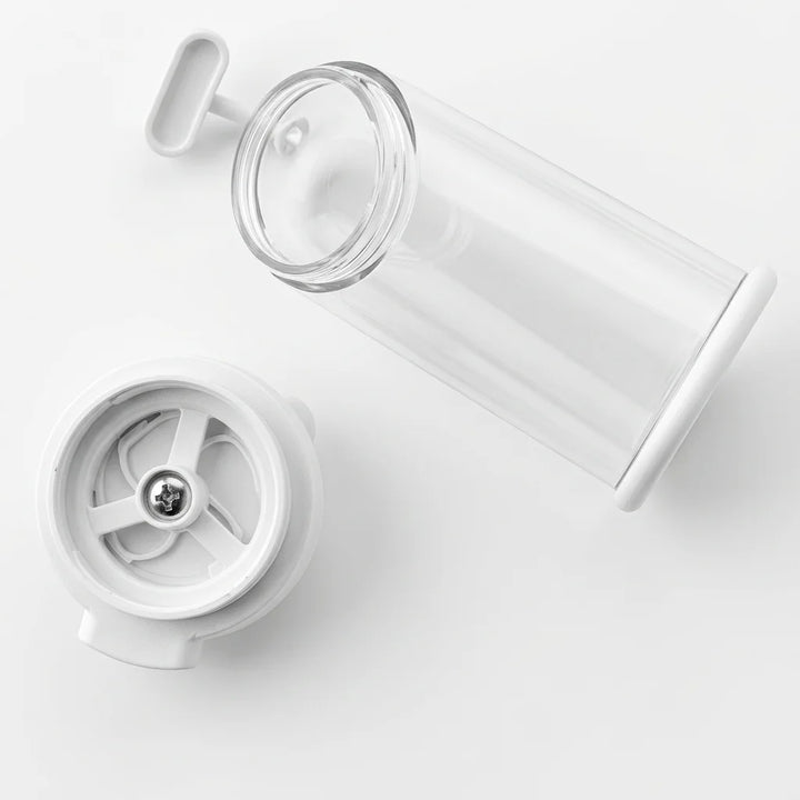 Zerlegtes weißes und transparentes Sesammühle. Es besteht aus einem liegenden transparenten Zylinder, einem weißen, runden Dosierteil mit sternförmigem Mechanismus und zentraler Schraube sowie einem kleinen weißen Hebel auf weißem Hintergrund.